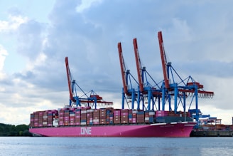 Large pink cargo ship with cranes at port.