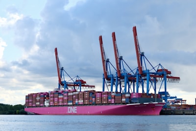 Large pink cargo ship with cranes at port.