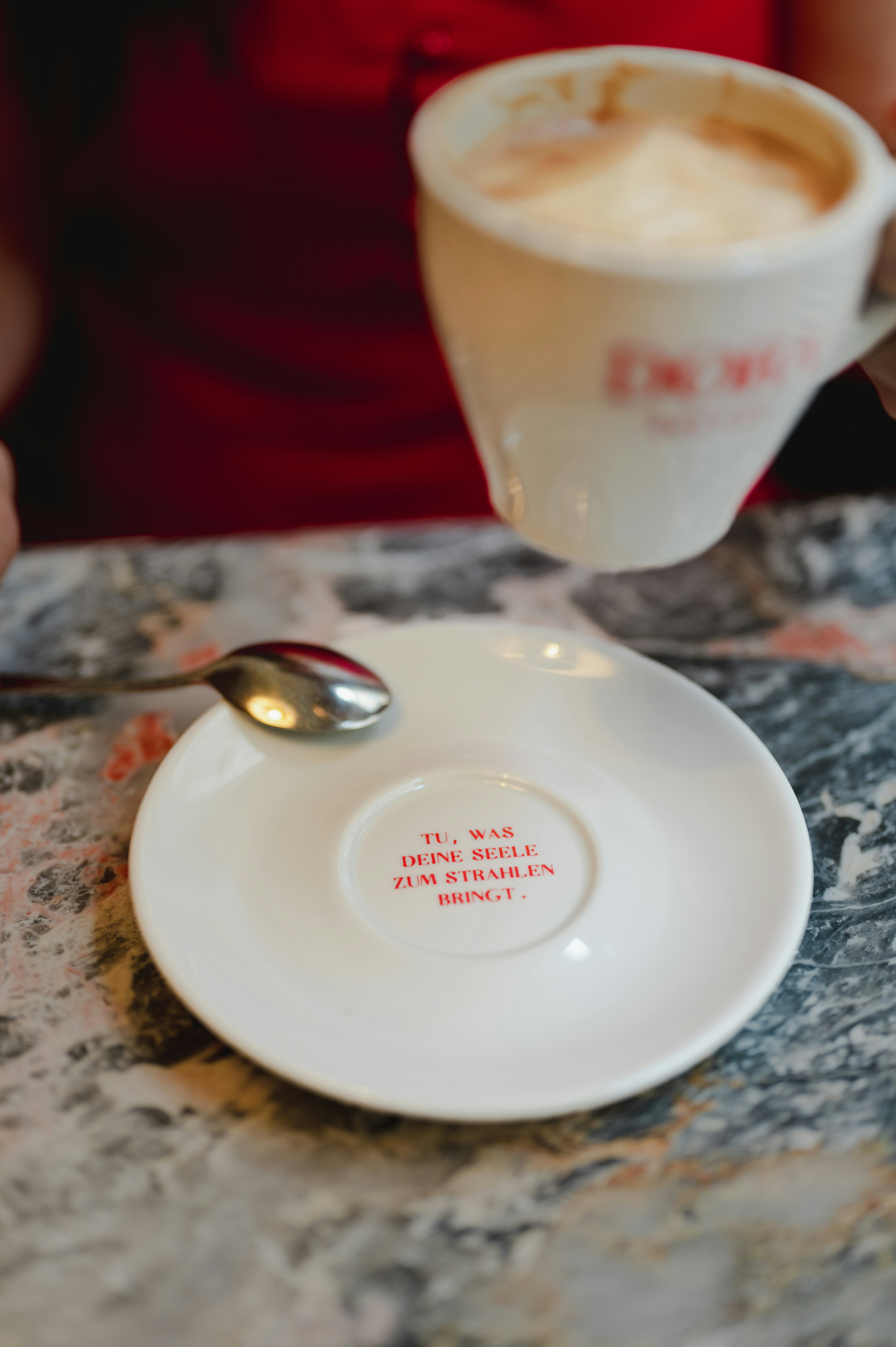 A hand holding a cup of coffee over a saucer.