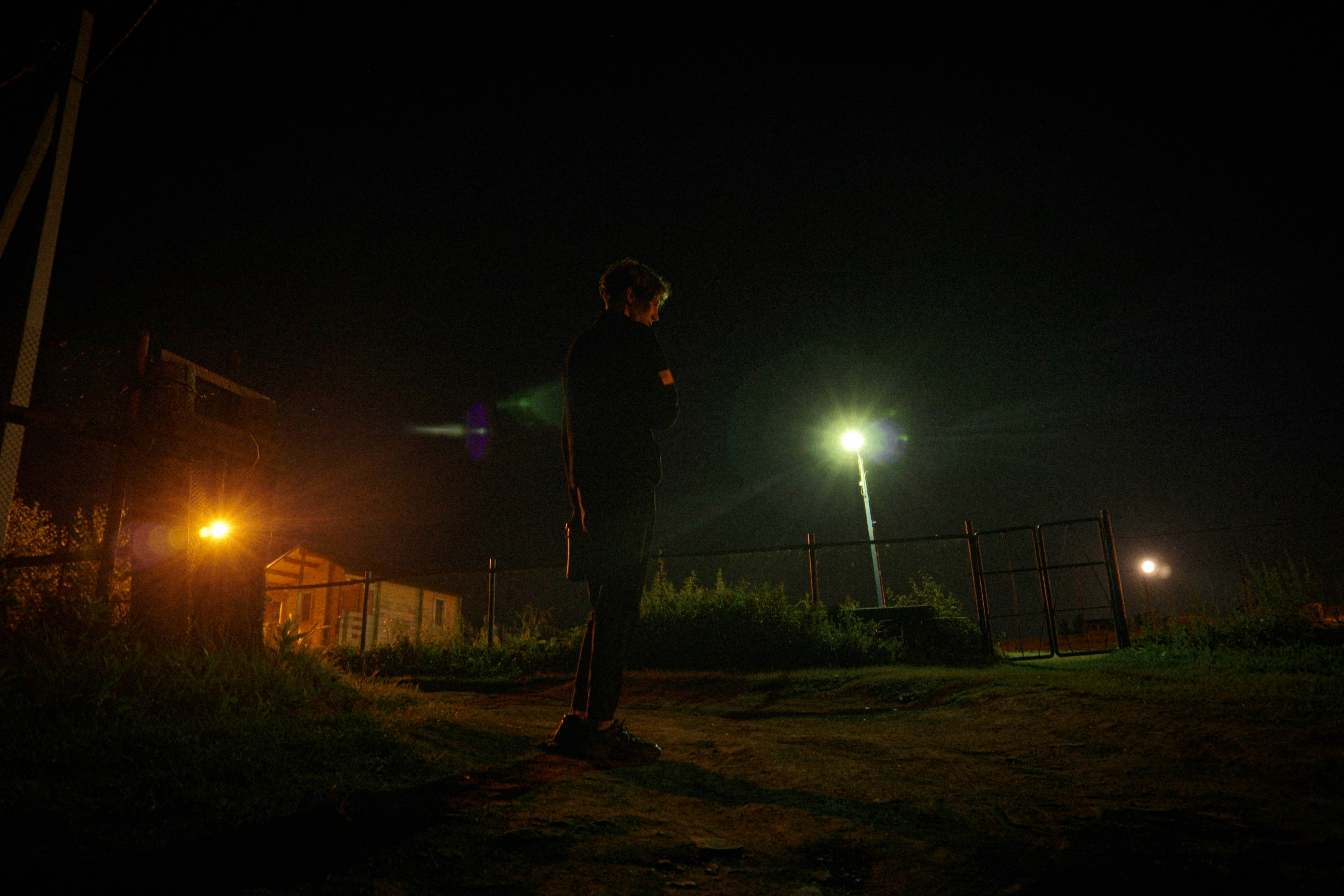 A lone person stands in the dark by streetlights.