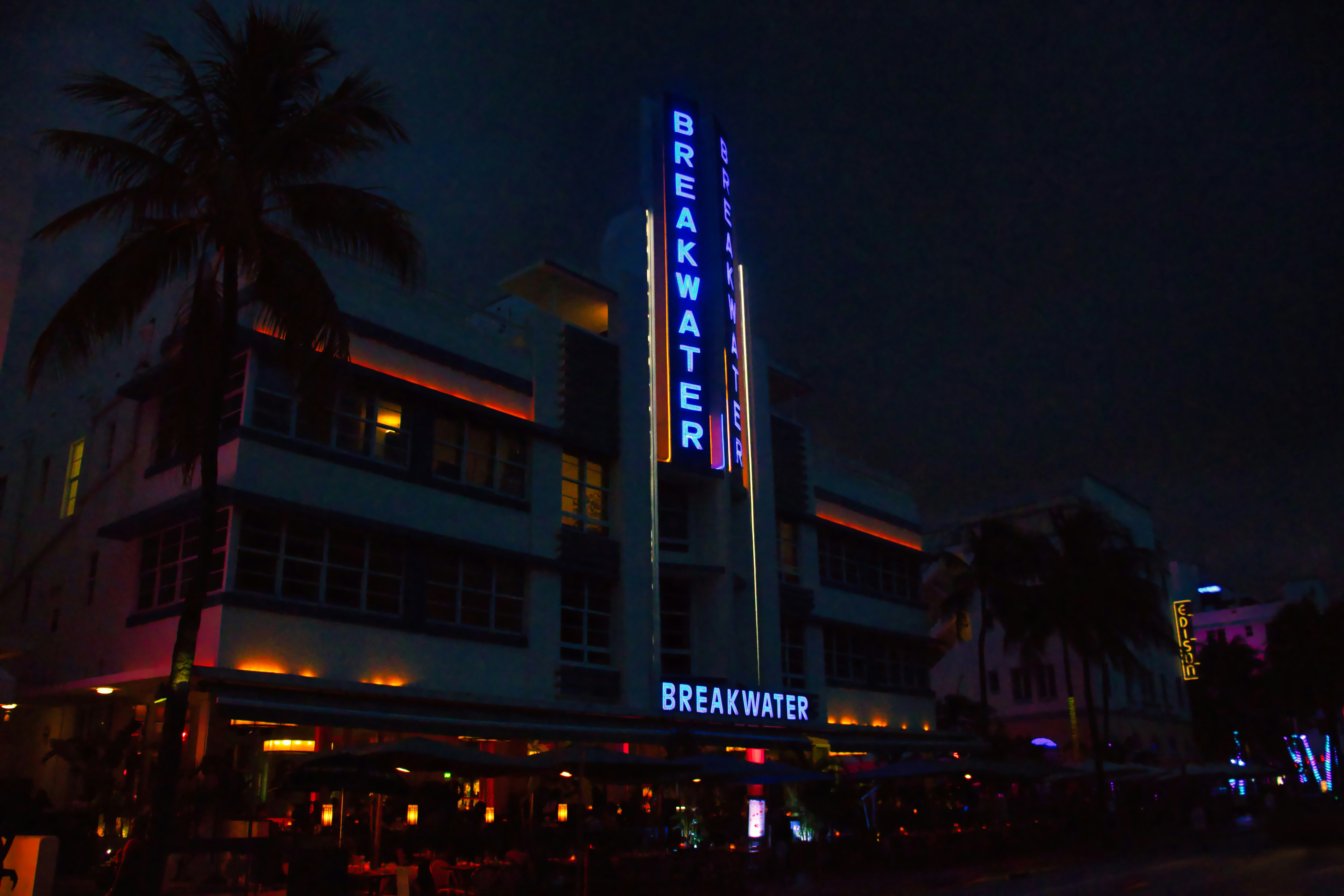 Art deco hotel lit up at night with neon signs.