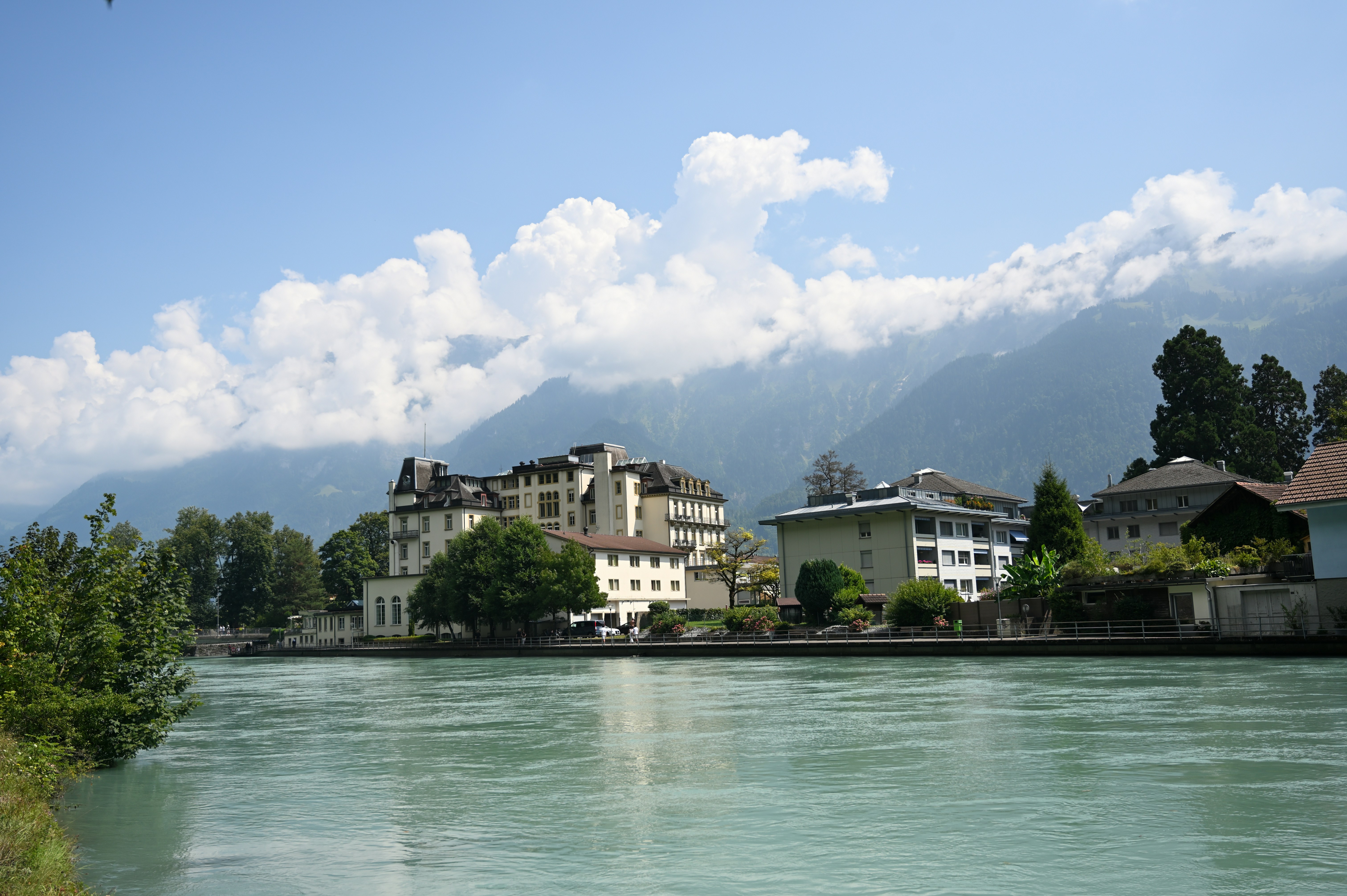Gli edifici costeggiano un ampio fiume con le montagne alle spalle.