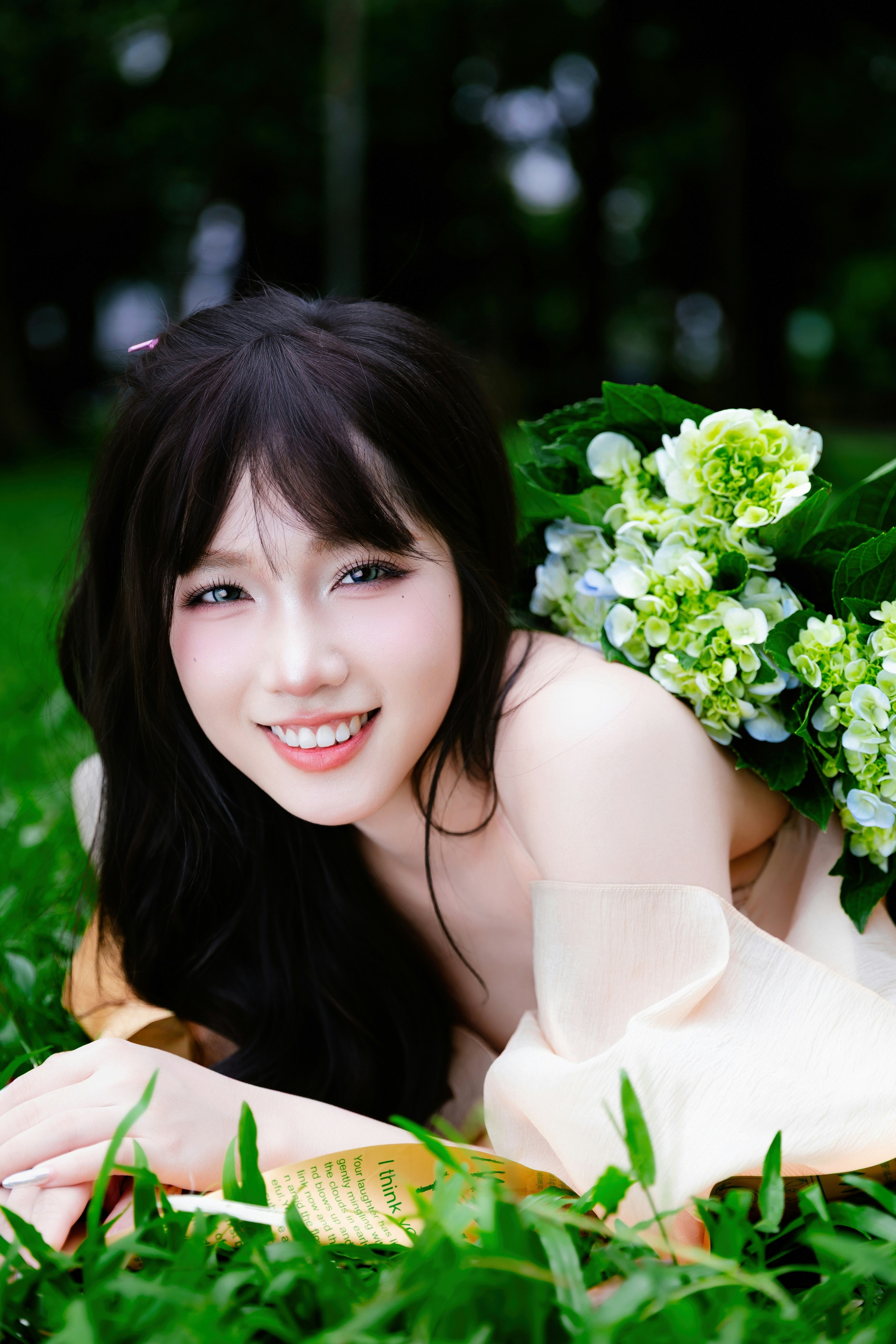 A smiling woman lies on grass with flowers