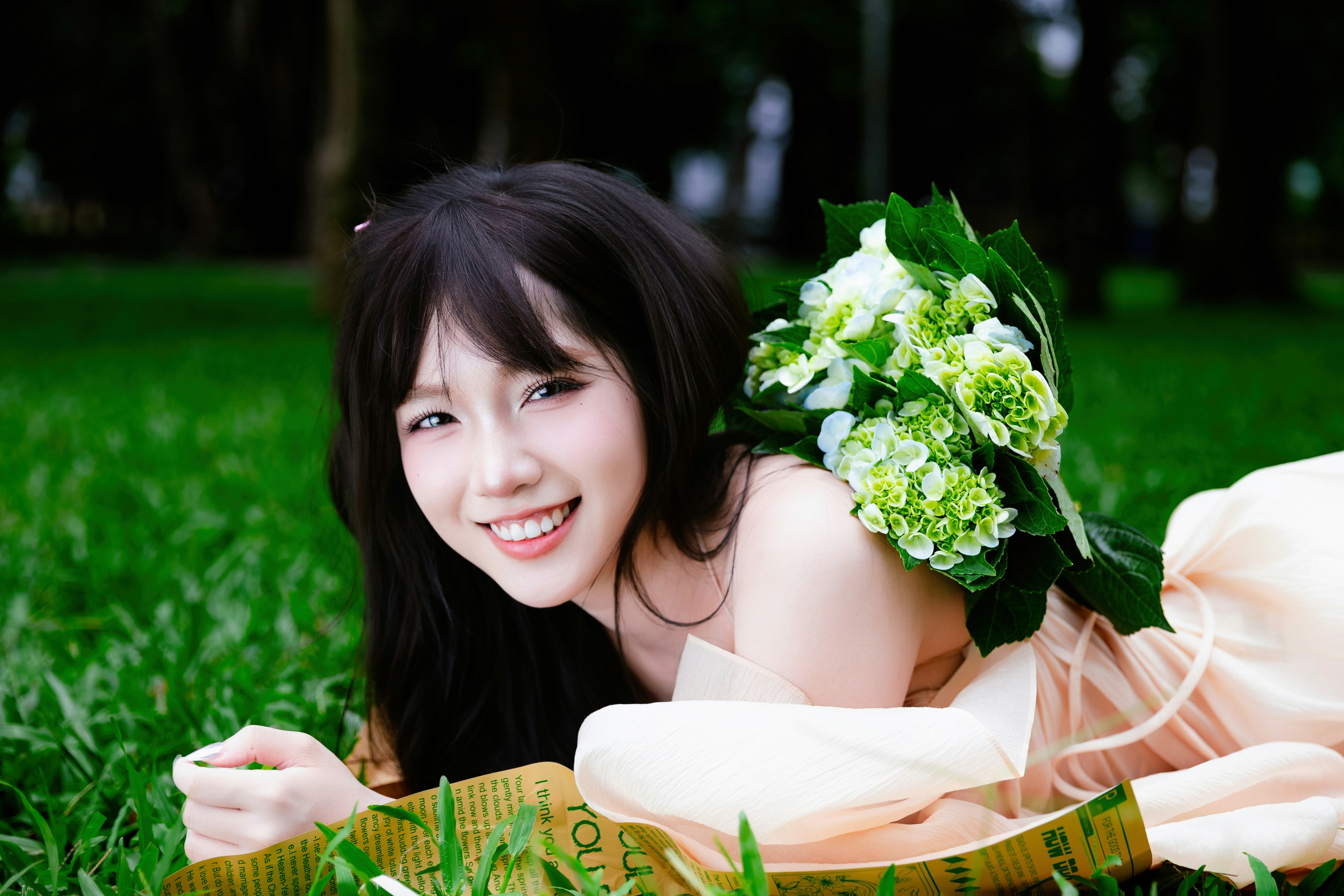 A young woman with a bouquet lies on green grass