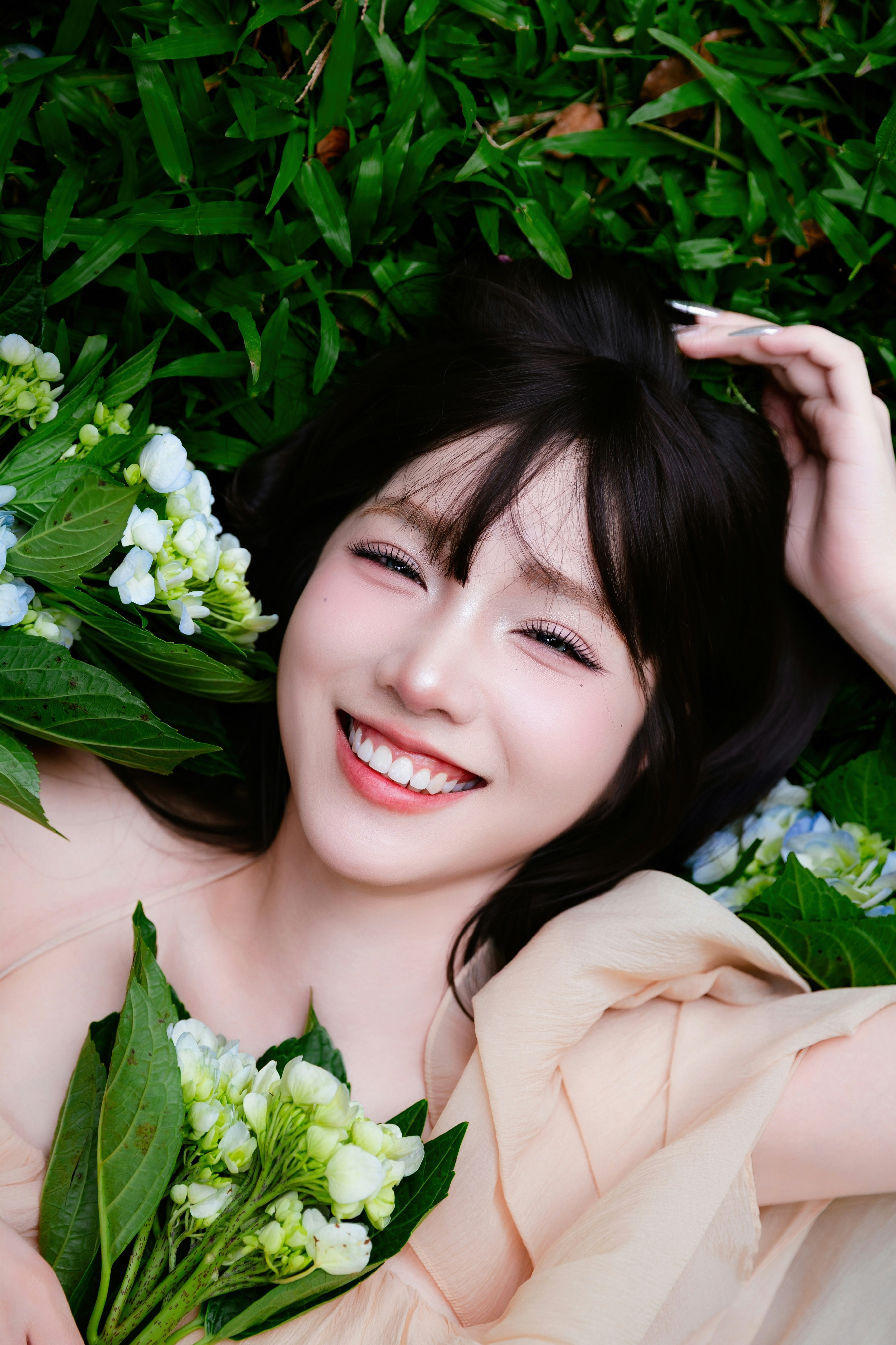 A smiling woman lies in grass with flowers.