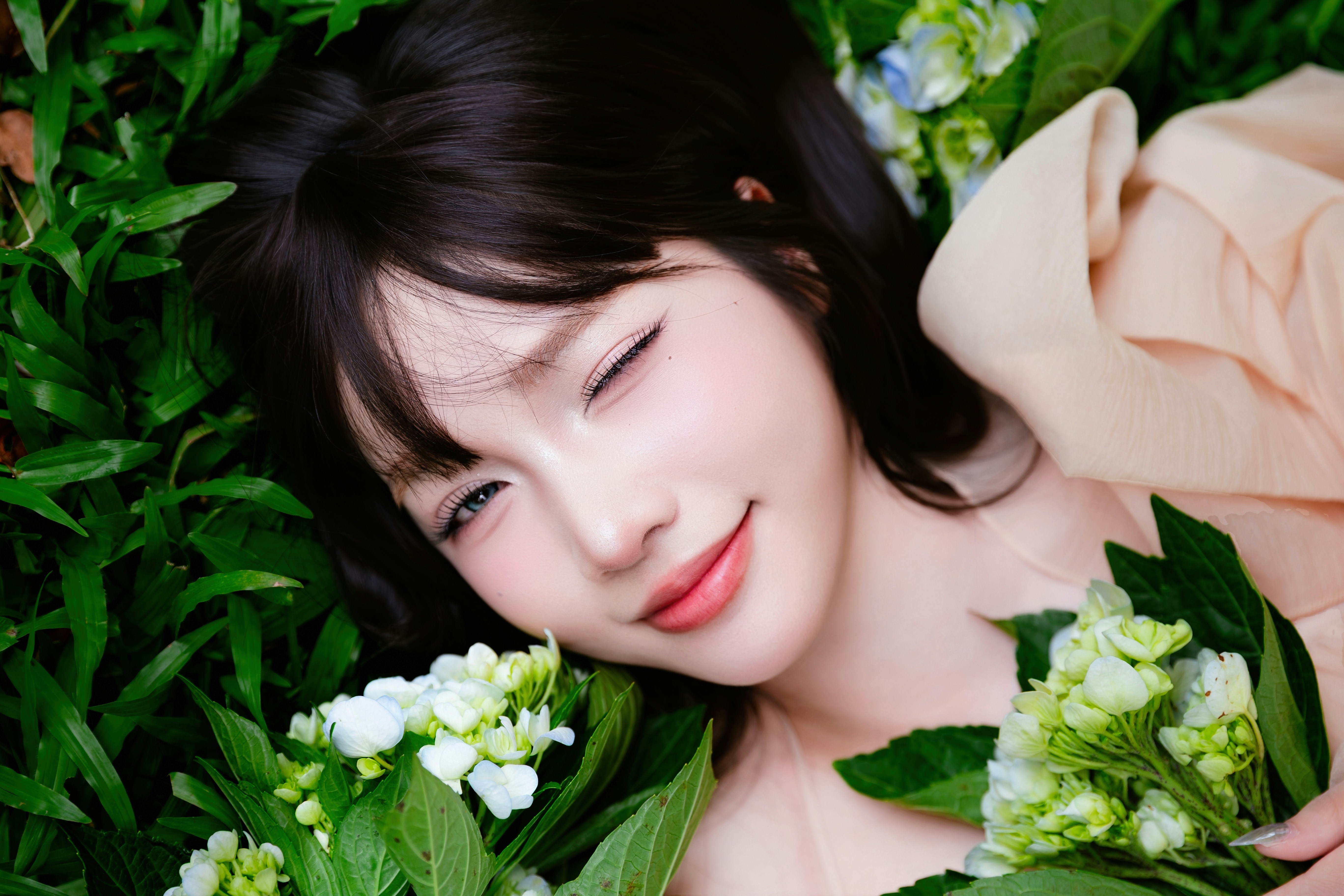 Young woman winks while lying among green leaves and flowers.