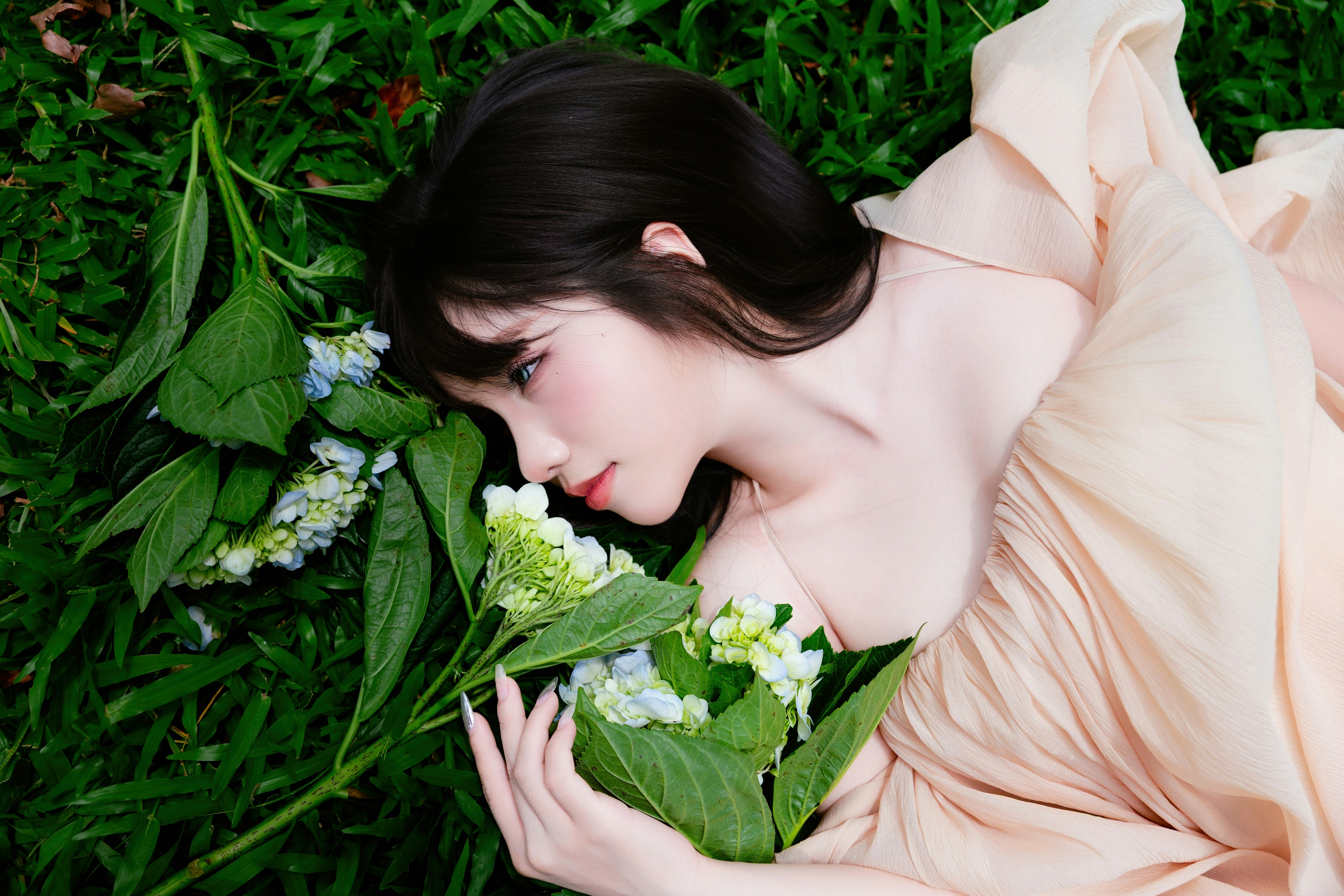 Smiling young woman lying on green grass with a bouquet of fresh hydrangea flowers