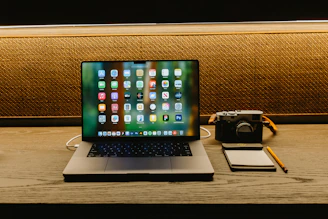 Laptop, camera, and notepad on a wooden desk.