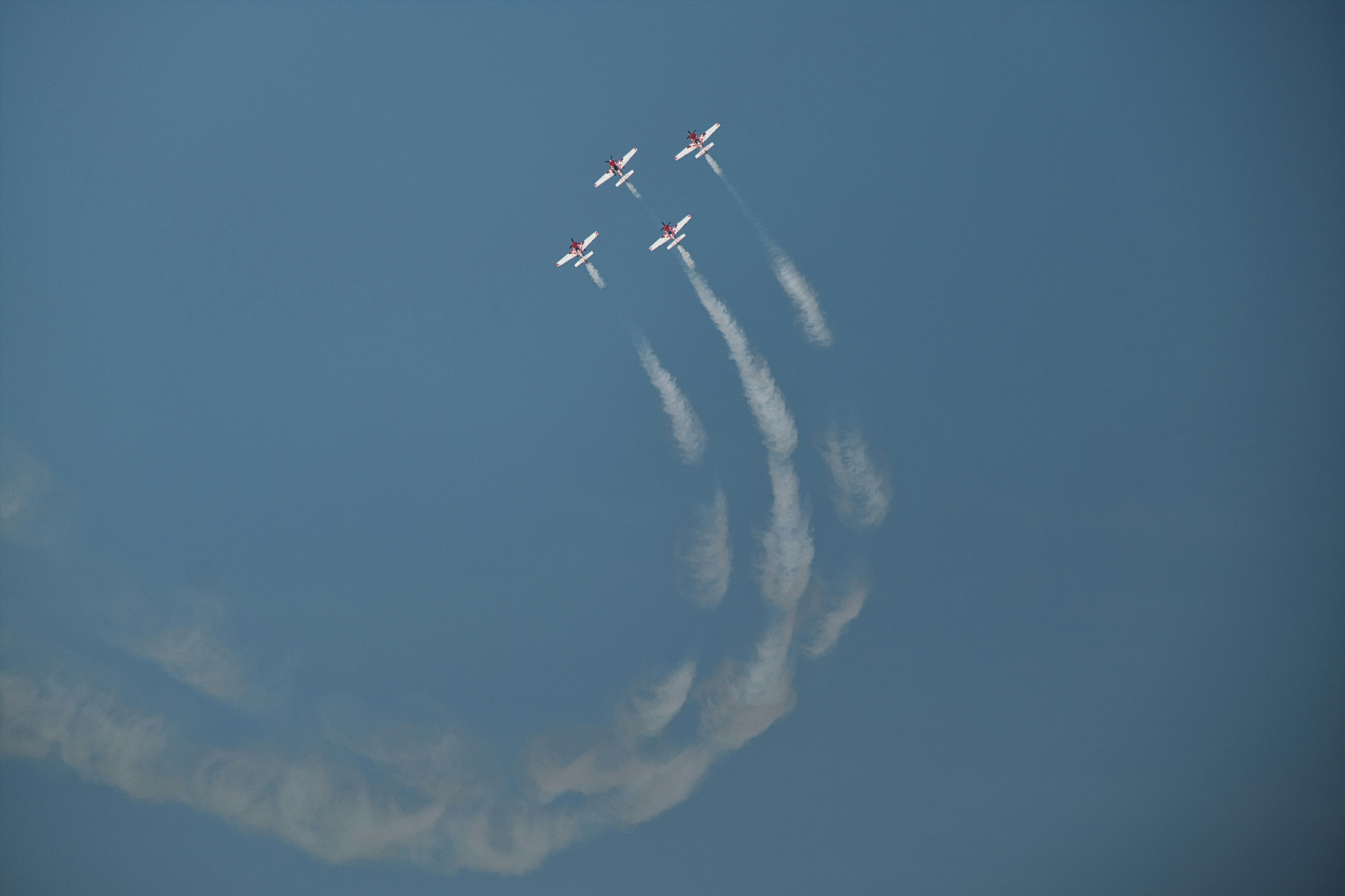 Cuatro aviones realizan acrobacias aéreas en un cielo azul claro.