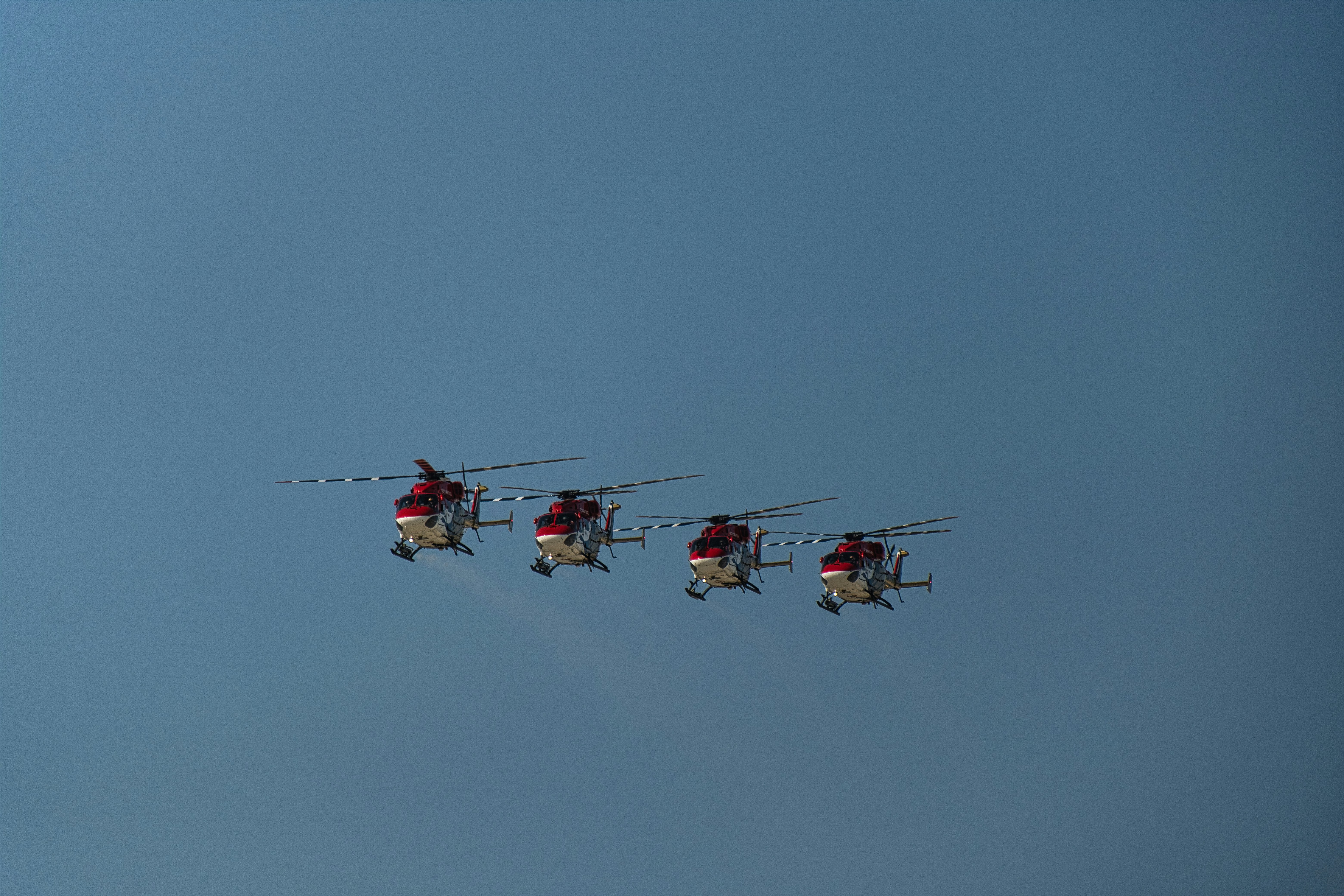 Cuatro helicópteros volando en formación contra un cielo azul claro.