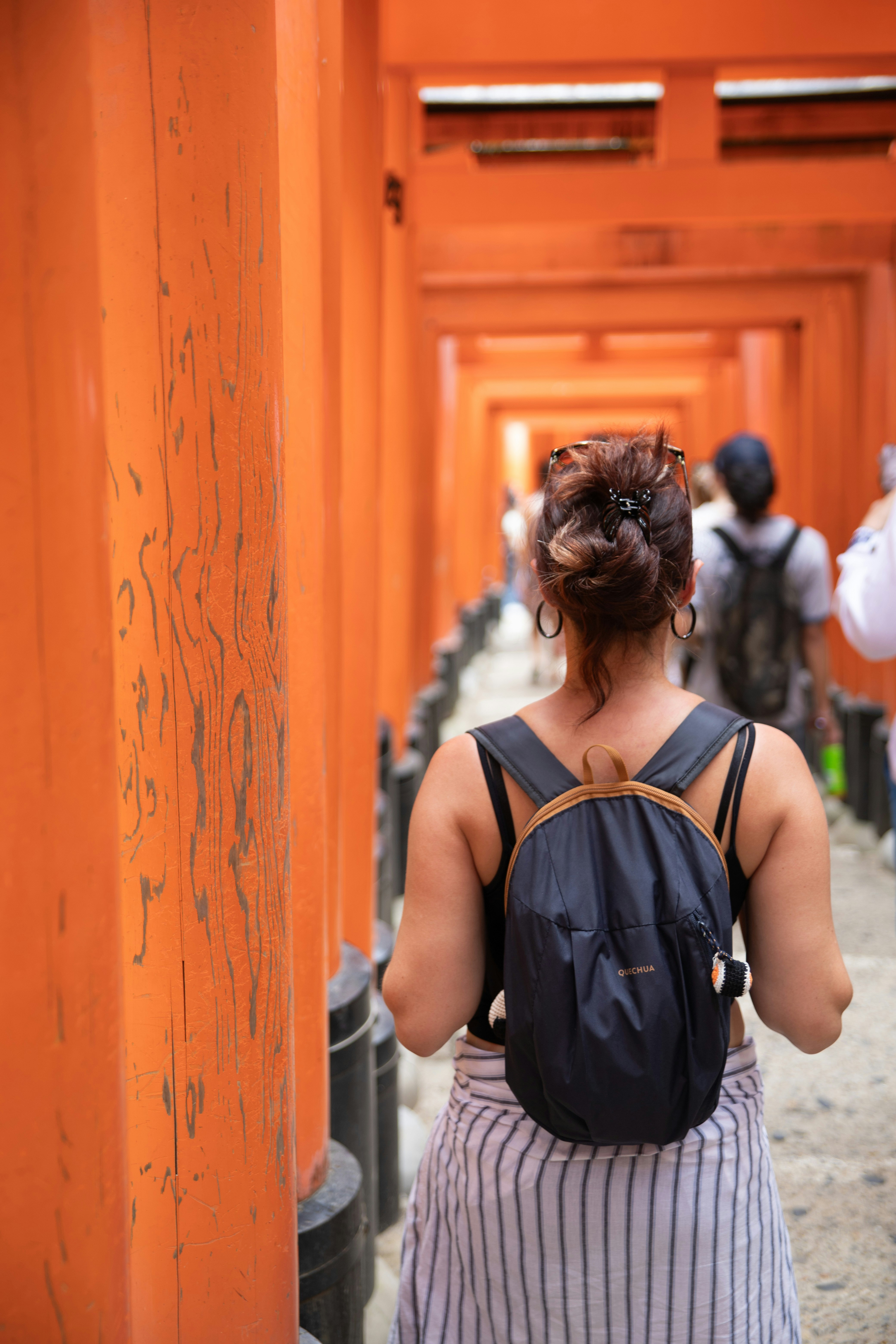 Woman walks through a tunnel of orange torii gates.
