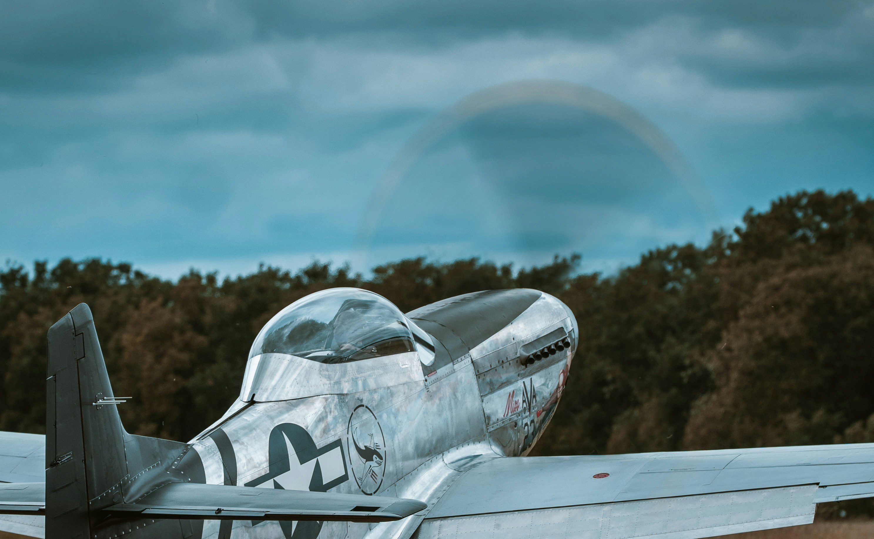Ein Oldtimer-Flugzeug mit sich drehendem Propeller vor bewölktem Himmel.