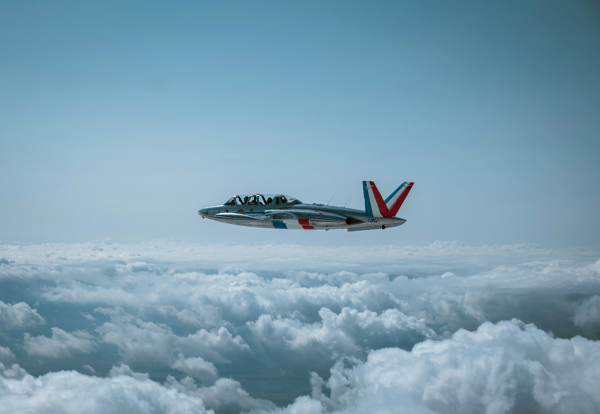 A jet airplane flies above fluffy white clouds.