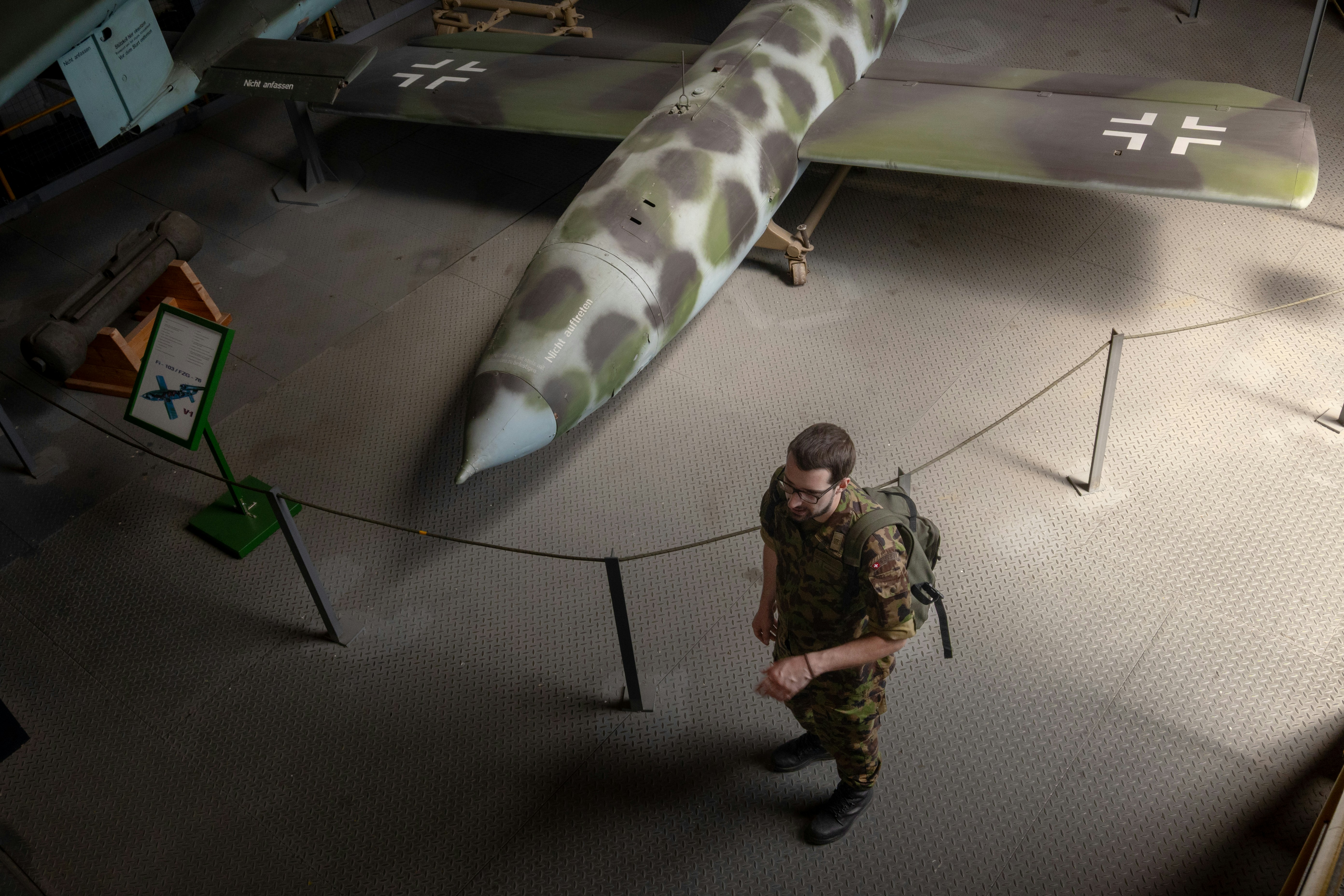 Man in camouflage uniform stands by a vintage airplane.