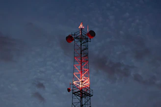 Cell tower illuminated with red lights against twilight sky