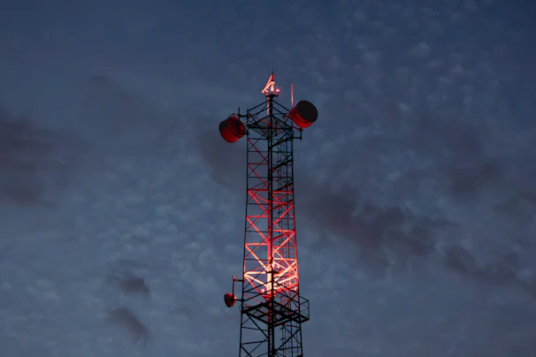Cell tower illuminated with red lights against twilight sky