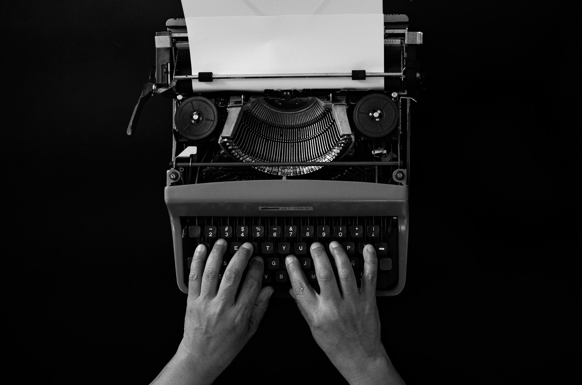 Hands typing on a vintage typewriter with paper.