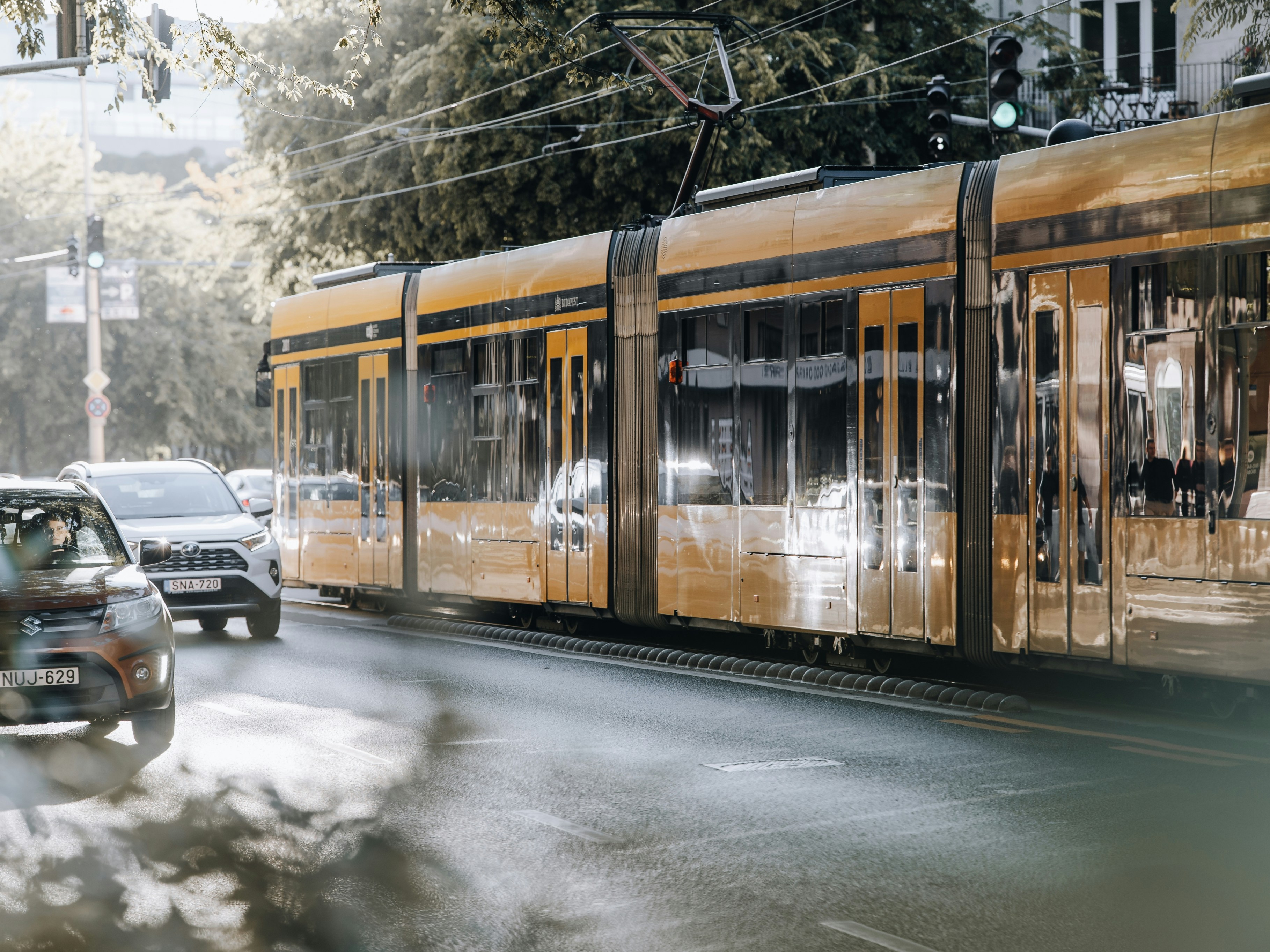 Yellow tram moving on city street with cars.