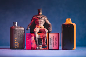 Batman figure sitting on vape packaging with devices