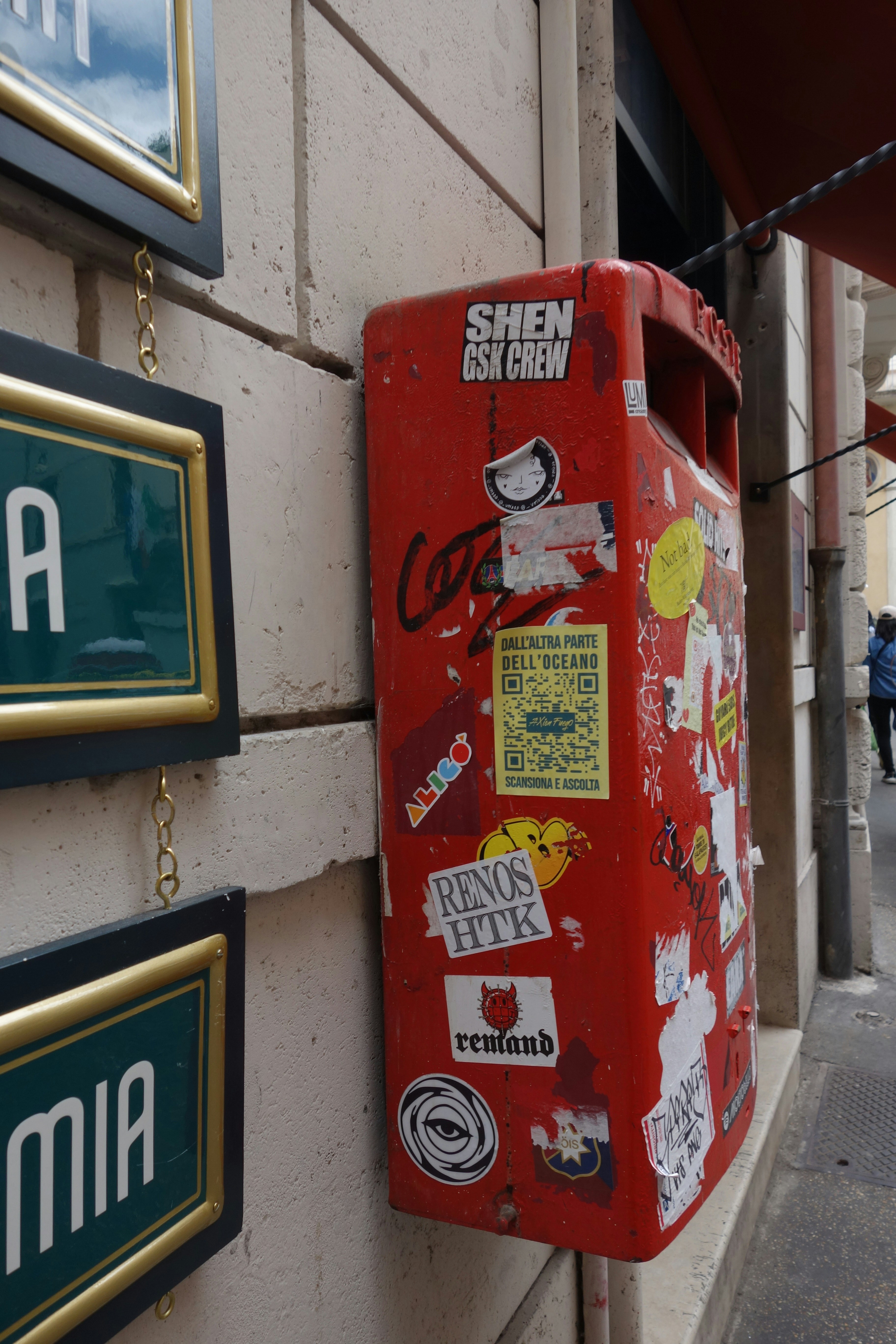 Red trash can covered in stickers on a wall.