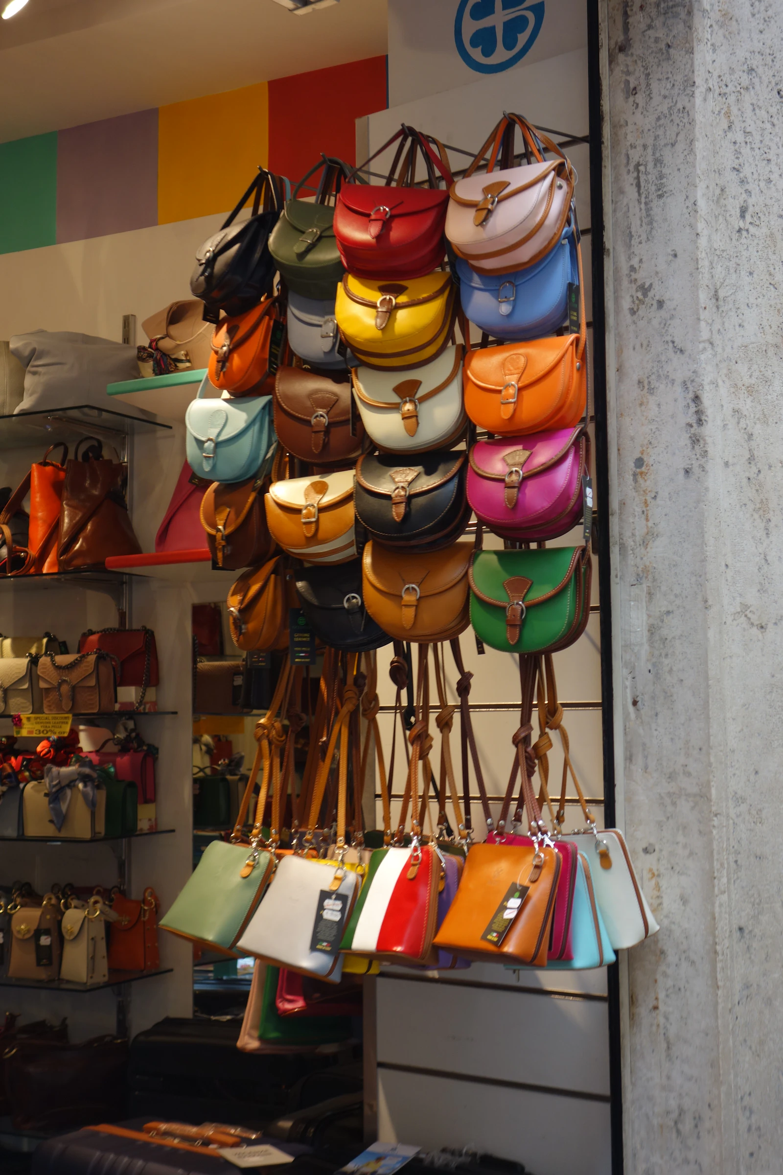 Wall display of dozens of colorful leather bags hanging in rows at a bag manufacturer showroom
