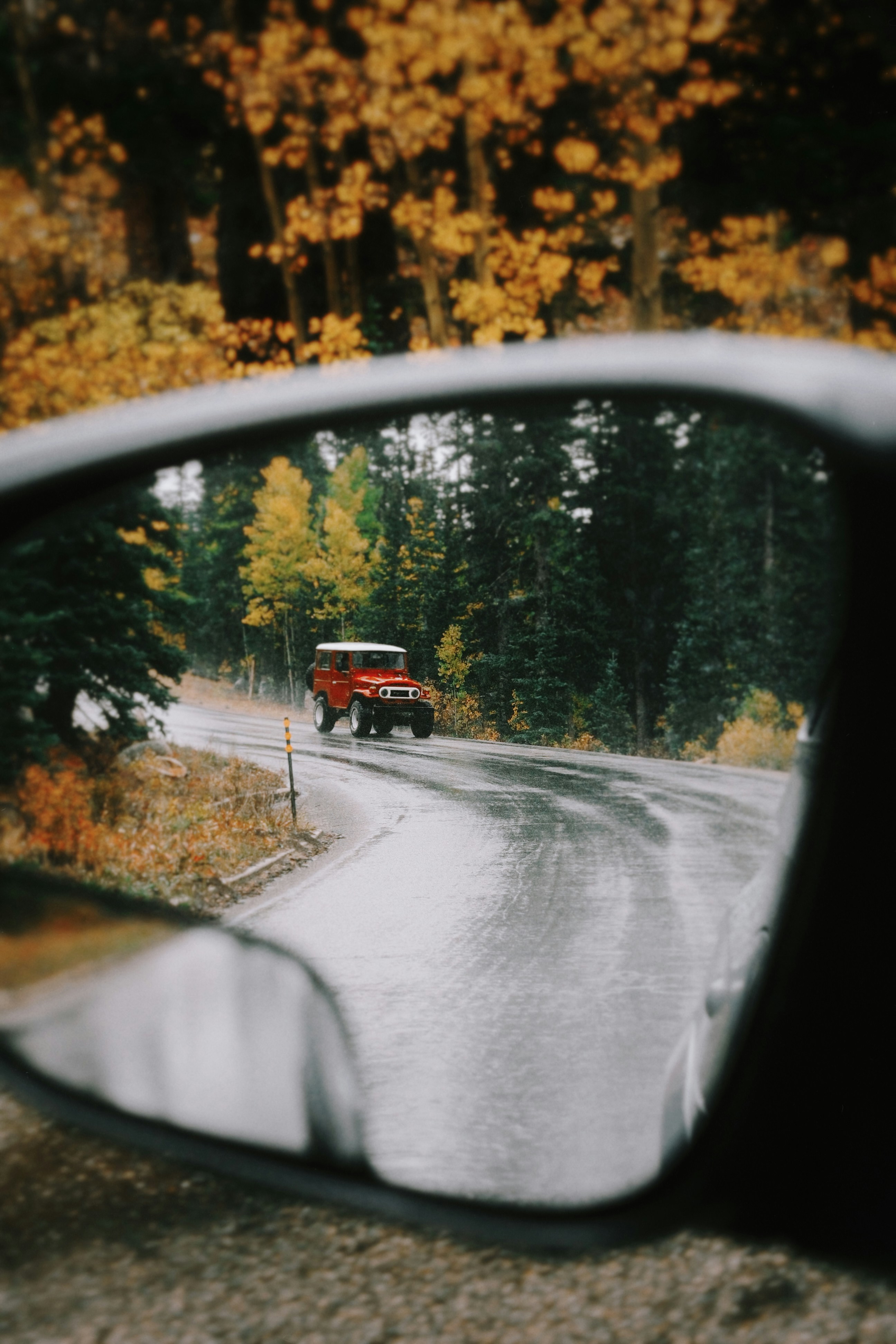Red vintage car driving on wet road through autumn forest