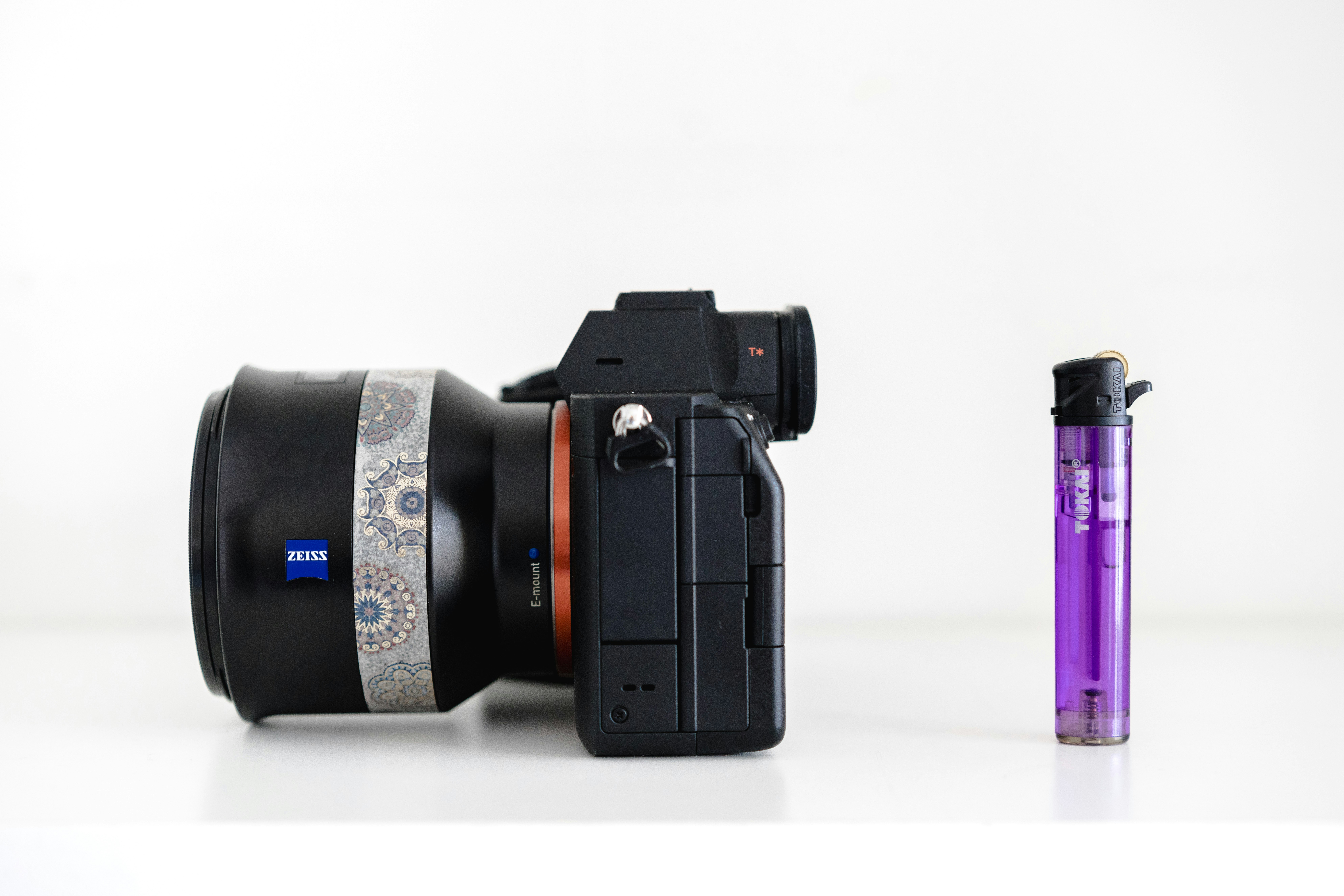 Camera lens and purple lighter on white surface