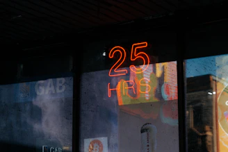 Neon sign with "25 hrs" reflects on glass