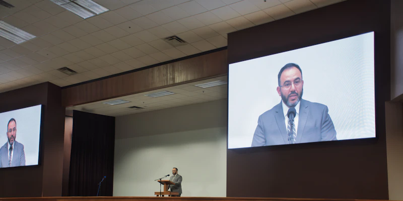 Speaker at a podium with a live video feed on screen