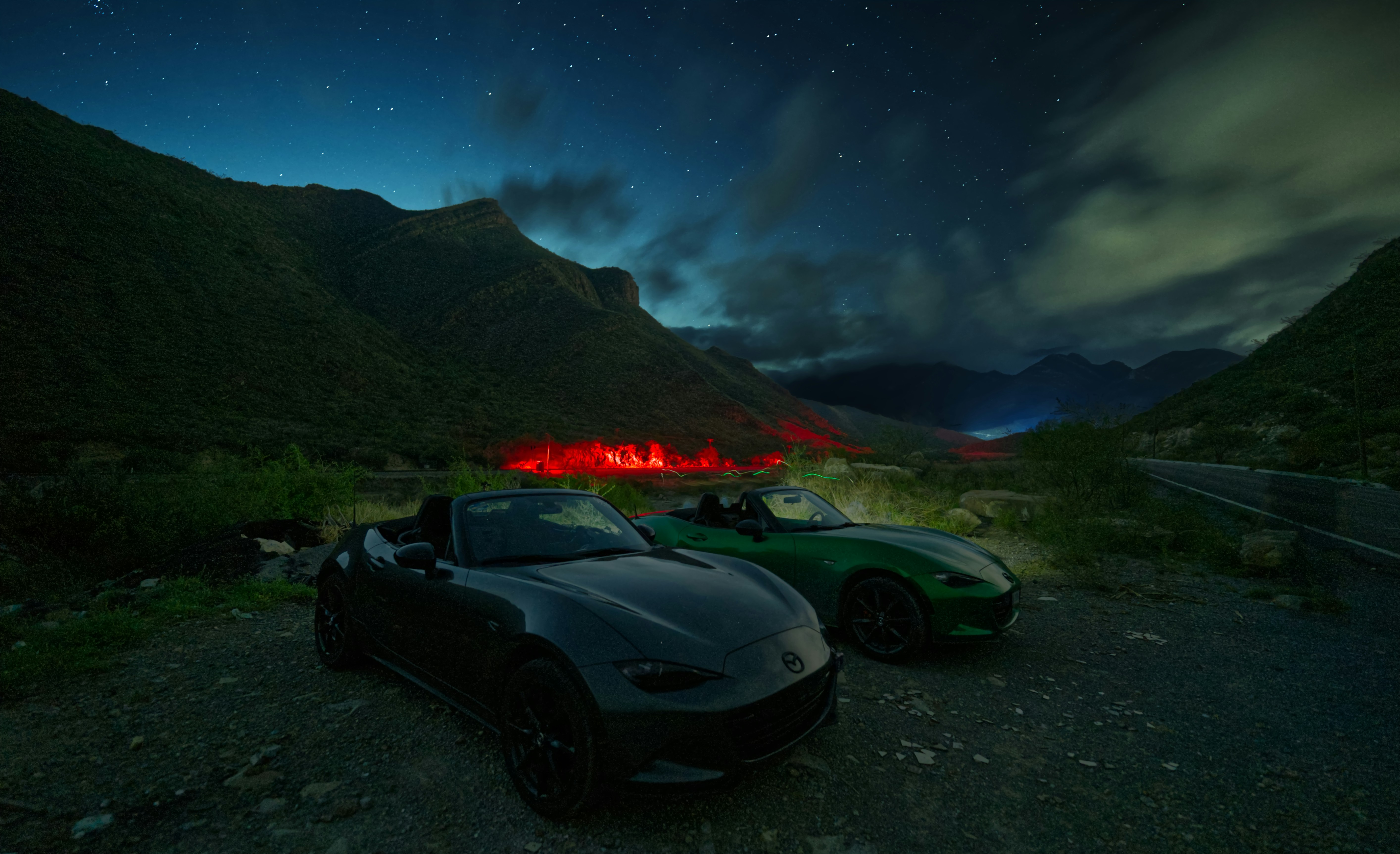 Dos autos convertibles estacionados por la noche con montañas.