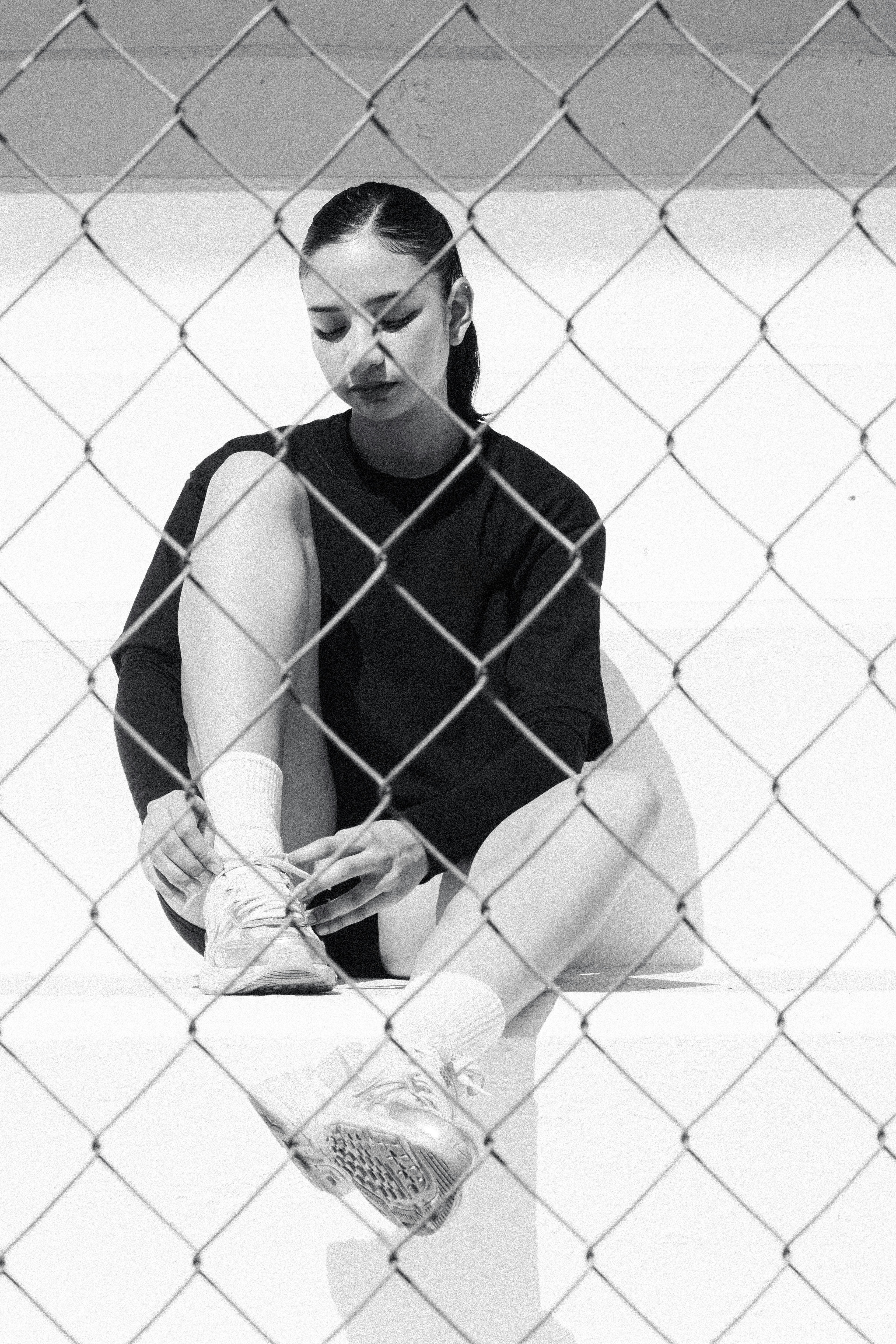 Woman tying shoelaces behind a chain-link fence