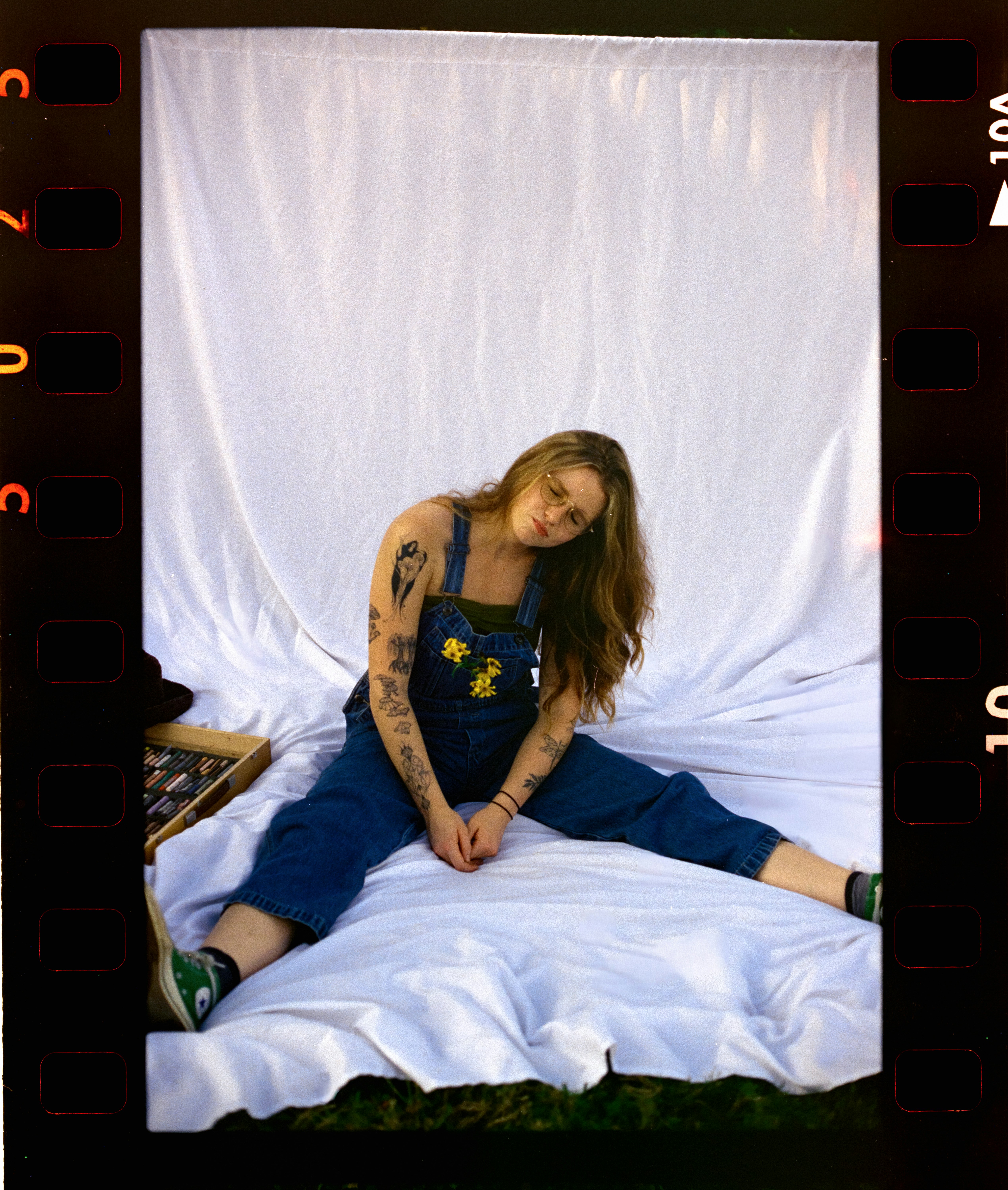 Young woman in blue overalls sitting on white fabric.