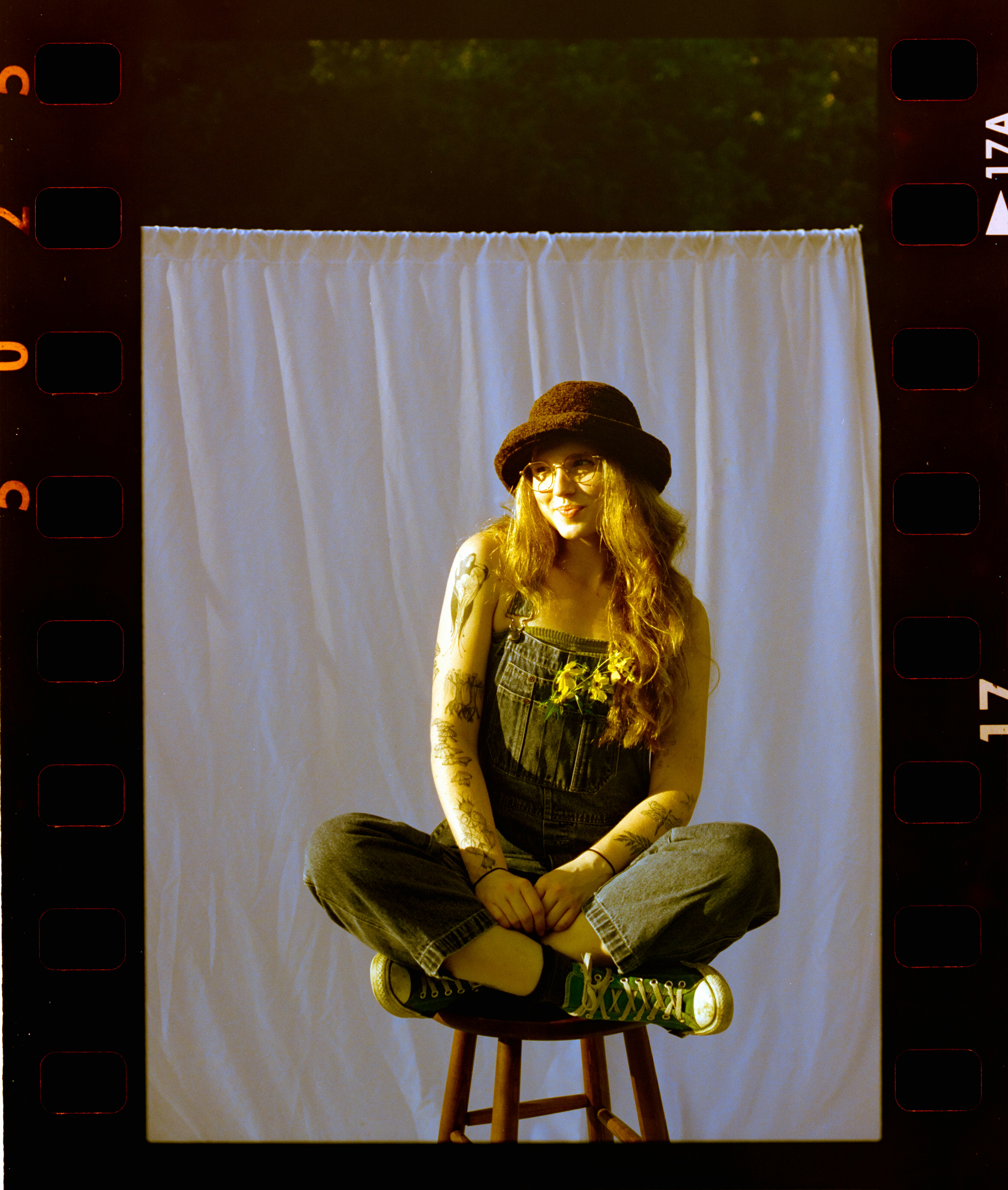 Mujer con mono y sombrero sentada con las piernas cruzadas.