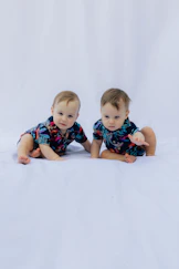 Two babies in matching floral shirts on white background
