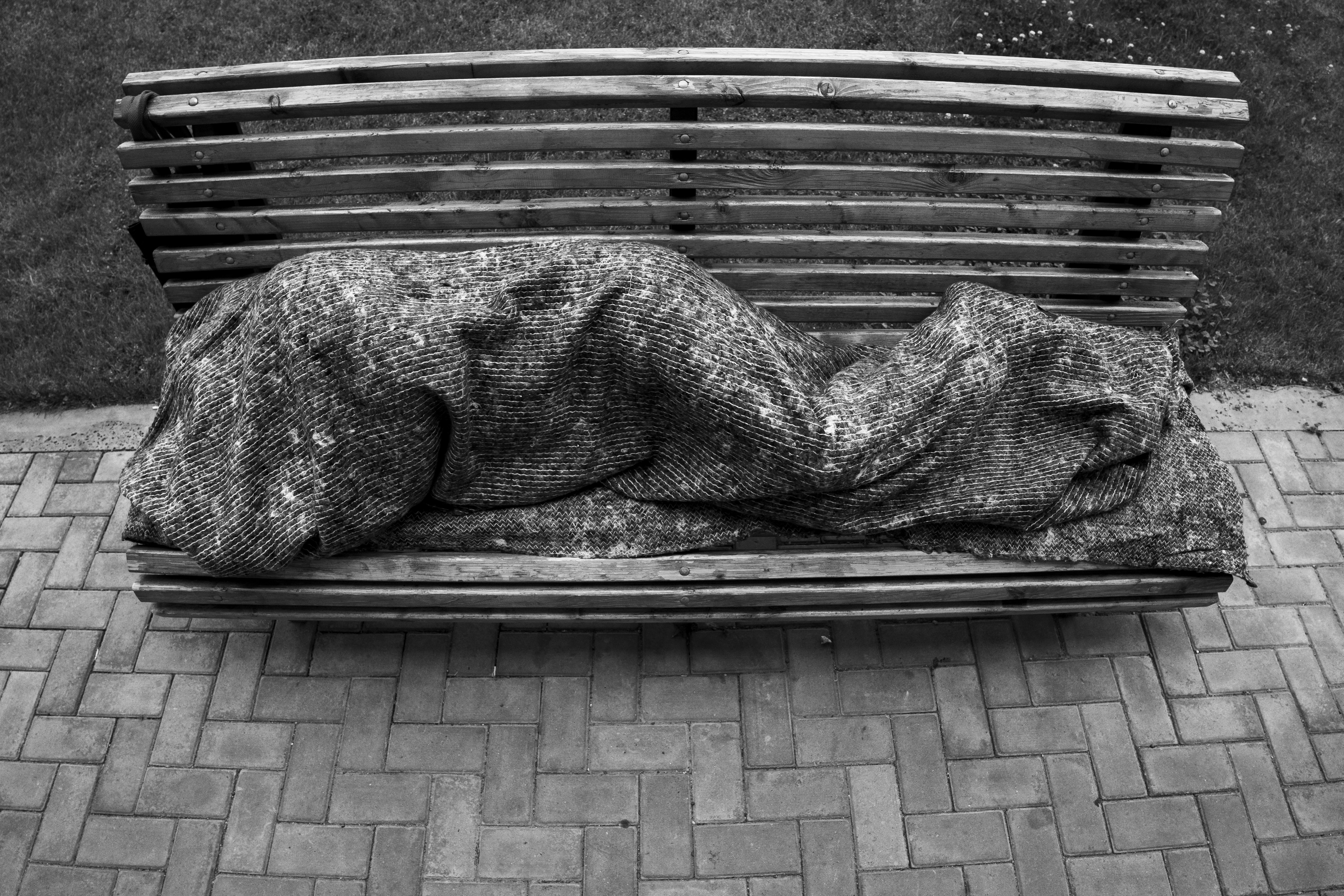 Stone sculpture of a figure sleeping on a park bench.
