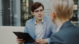 Man in suit holding clipboard talking to woman