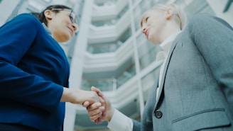 Two businesswomen shaking hands in a modern office building.