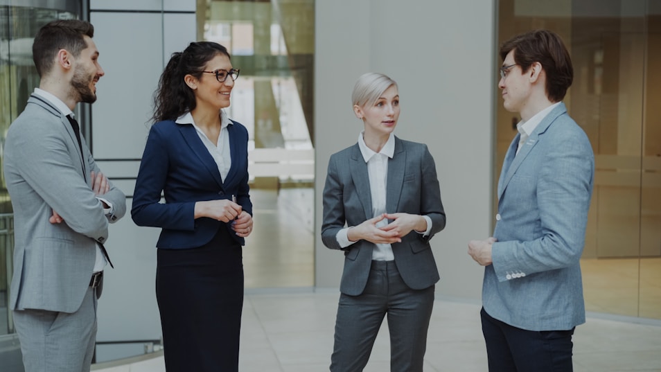 Four business professionals conversing in a modern office lobby.