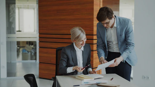 Two colleagues discussing documents at an office desk.