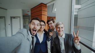 Four colleagues taking a selfie in an office hallway.