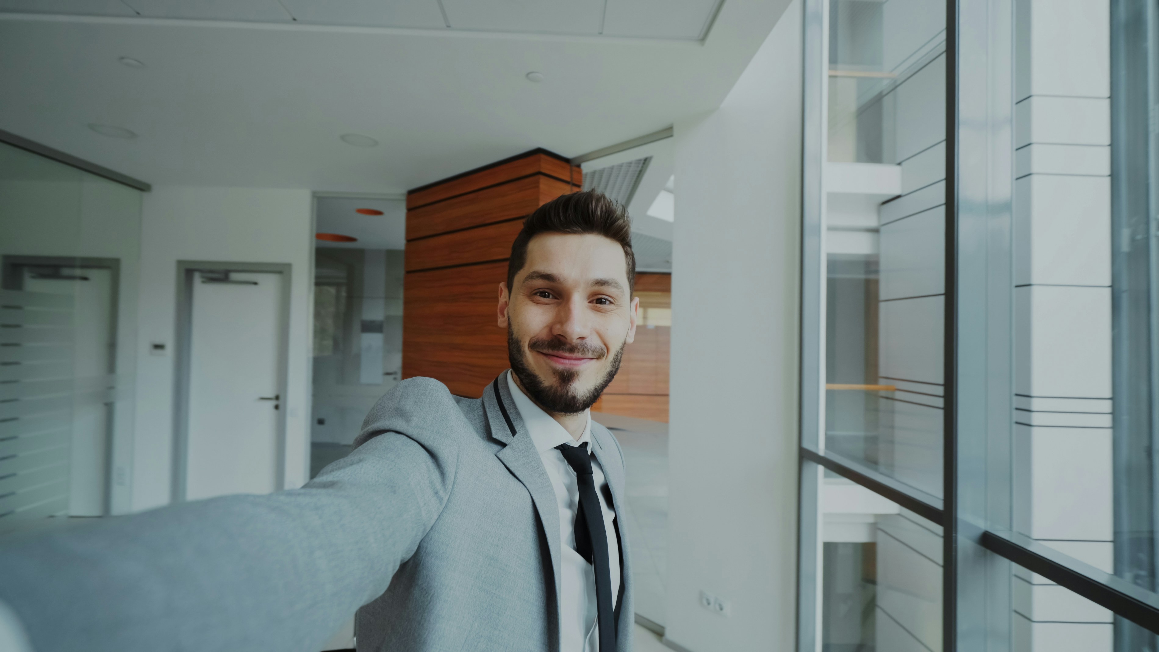 Man in suit taking a selfie in modern office hallway