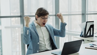 Man in suit celebrating success at office desk.
