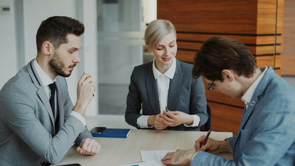Personas firmando un documento en una mesa de negocios
