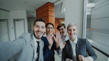 Four business people smiling and waving at camera.