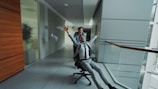 Man in suit rides office chair pushed by colleague