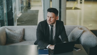 Man in suit sitting with laptop on couch.