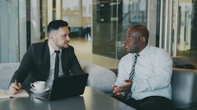 Two businessmen in suits talking in a modern office.