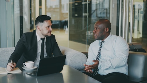Two businessmen in suits talking in a modern office.