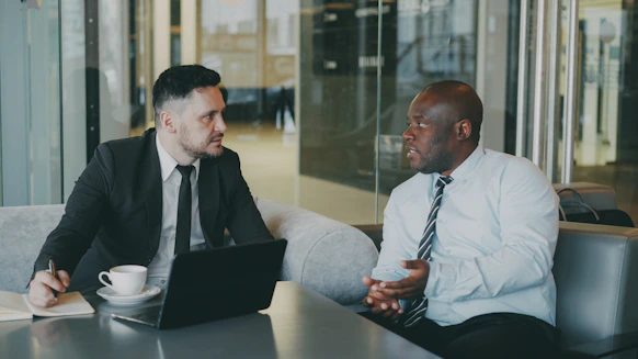 Two businessmen in suits talking in a modern office.