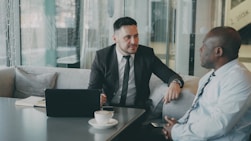 Two businessmen talking at a table with laptop.